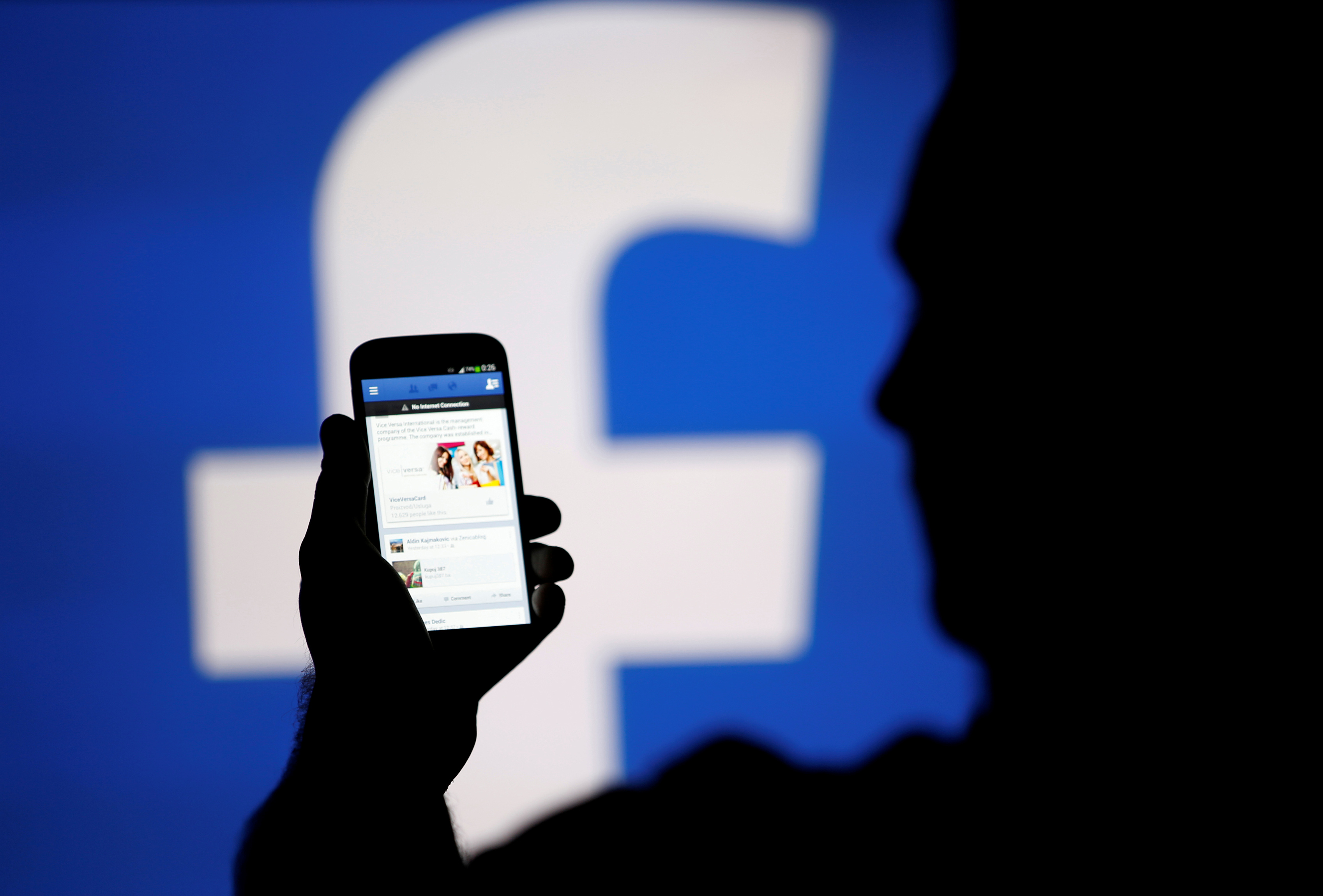 A man is silhouetted against a video screen with a Facebook logo as he poses with a smartphone in this photo illustration taken in Zenica